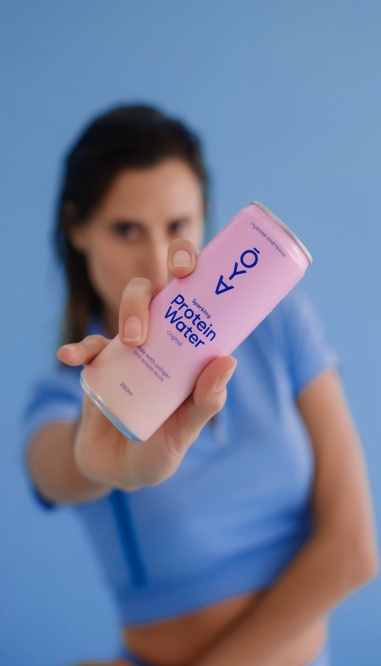 Woman holding a pink ŌYA Sparkling Protein Water can
